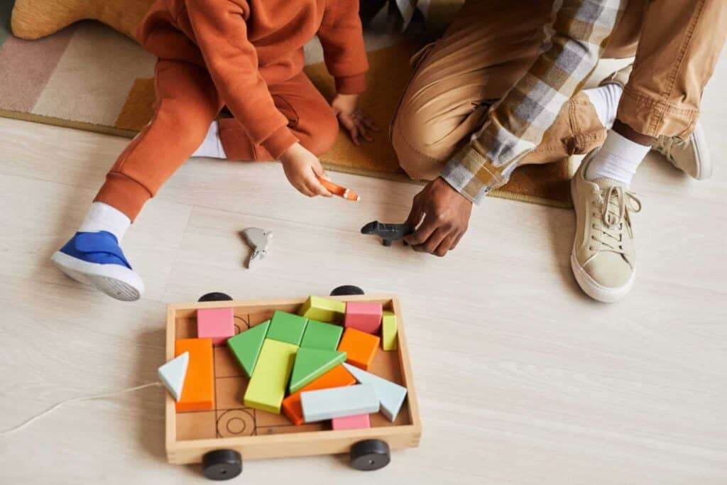 Playing with colorful building blocks on a wooden floor with a child and adult.