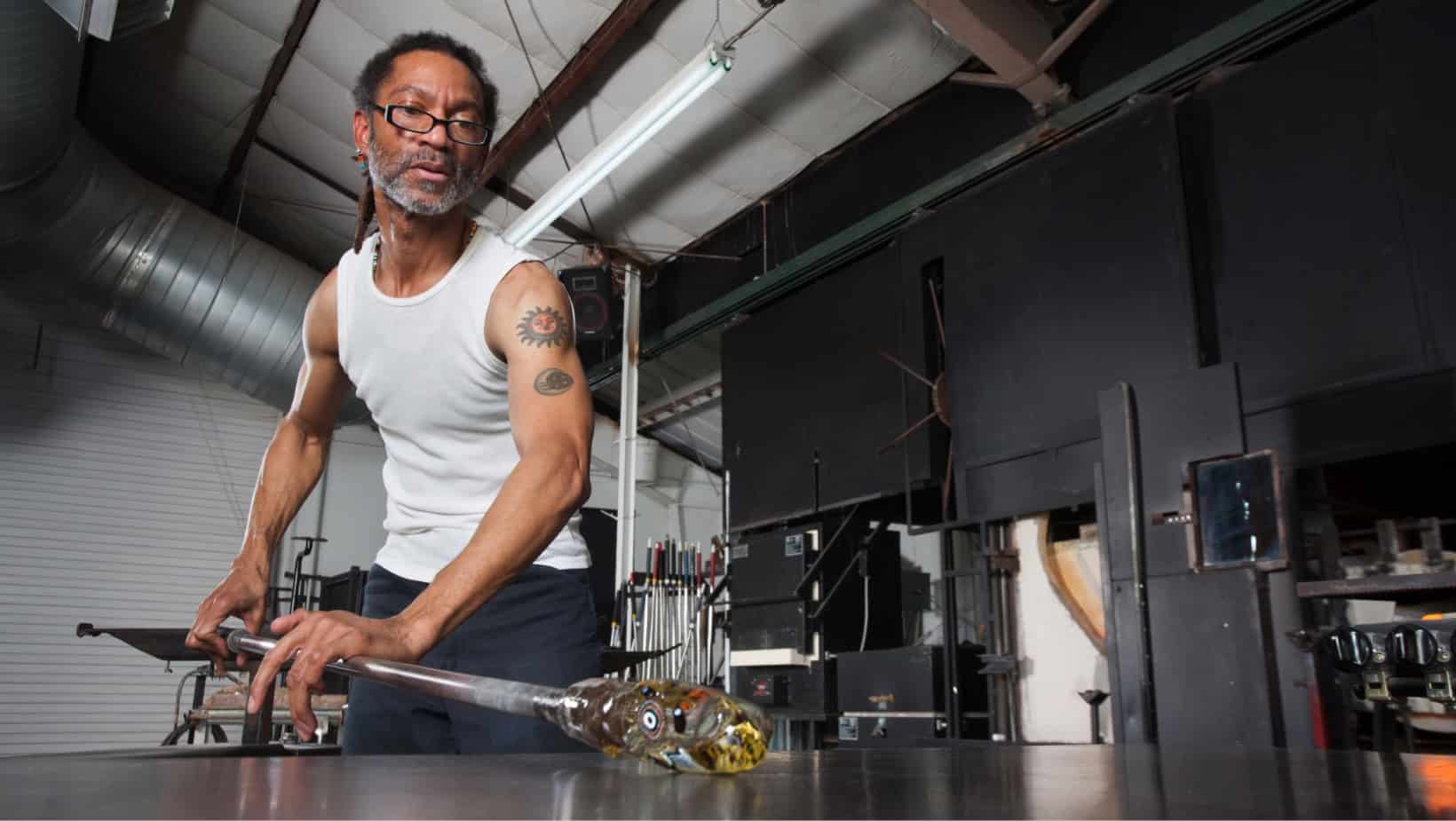 Black man working with glassblowing tools in a studio setting.