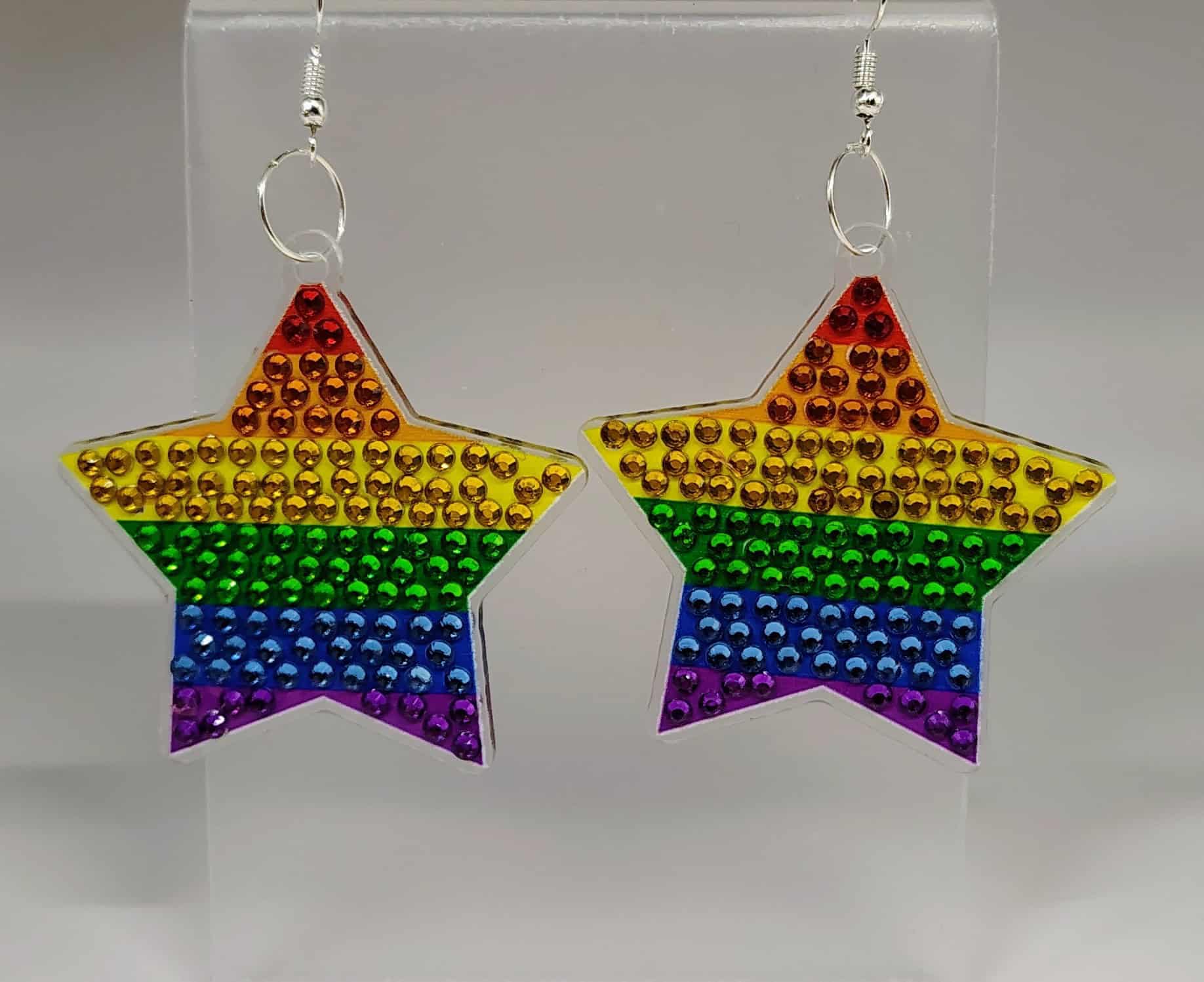IMG_20250406_144815670_HDR_AE Rainbow star-shaped earrings with colorful rhinestones on a clear display stand.