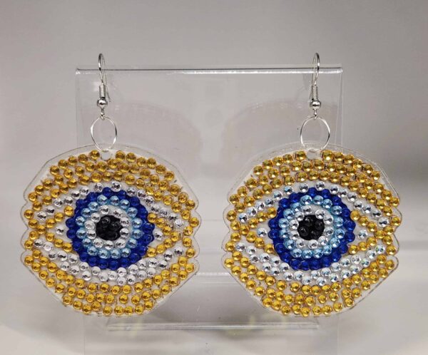 Golden and blue beaded eye-shaped earrings with silver hooks, displayed on a clear stand.