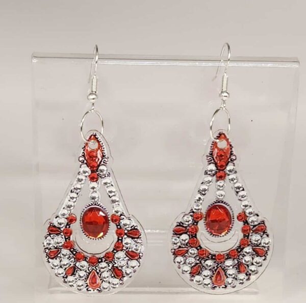 Red gemstone and silver dangle earrings with intricate design, displayed on a clear stand.