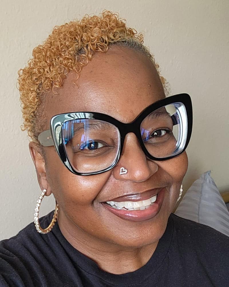 Black woman smiling with glasses, curly blonde hair, and hoop earrings, representing BlackSpace comm.