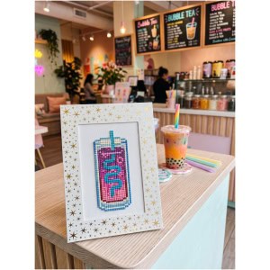 Colorful bubble tea cross-stitch art on a cafe table.